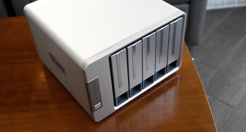 Angled view of a silver TerraMaster NAS device with five drive bays, placed on a wooden surface.