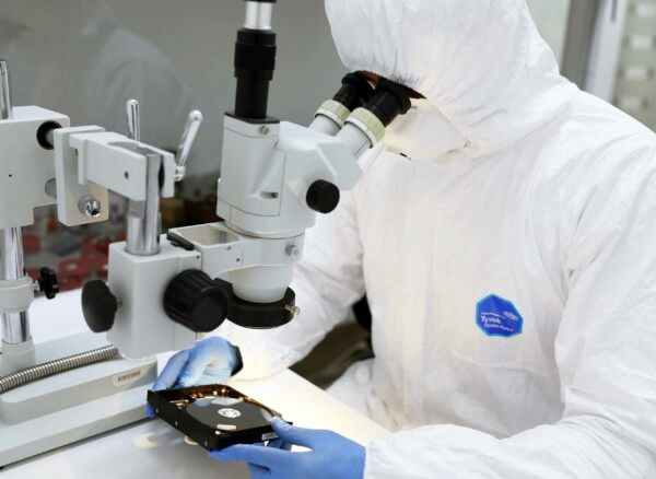 Technician in cleanroom performing data recovery on a storage device with specialized equipment.