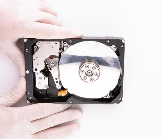 Technician in cleanroom inspecting HDD under microscope for data recovery.