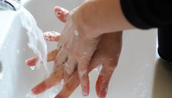 Person washing hands with soap under running water at a sink.